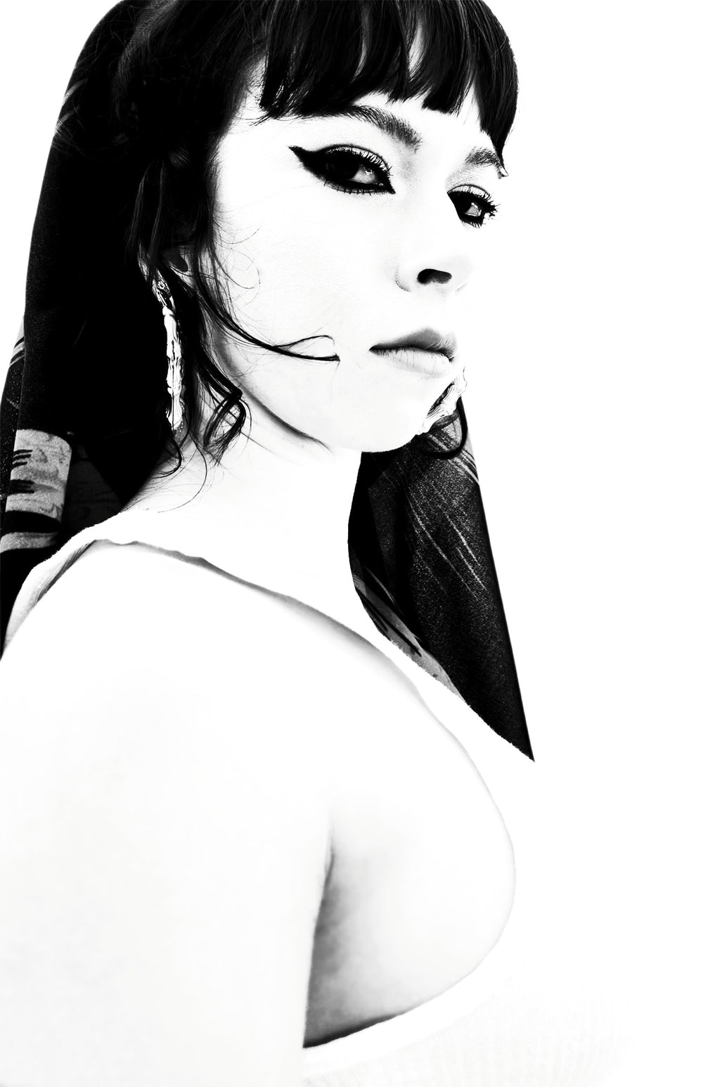 Black and white portrait of a woman with dark hair, winged eyeliner, and a white top against a white background.