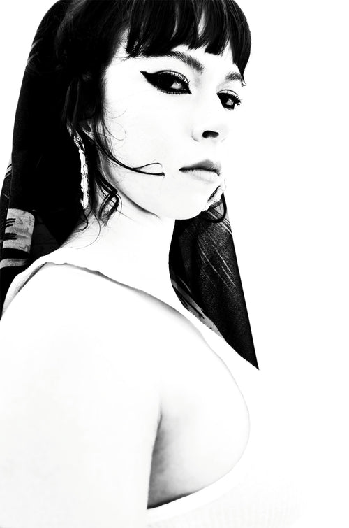 Black and white portrait of a woman with dark hair, winged eyeliner, and a white top against a white background.